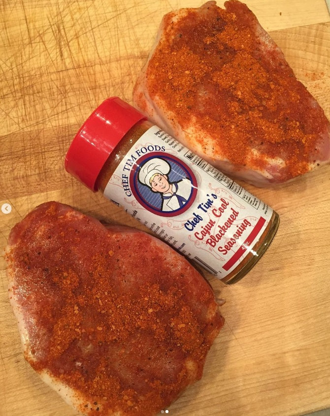 Two Pork Chops on a cutting board and seasoned with Chef Tim's Cajun Cool Blackened Seasoning.  A delightfully mild (4 out of 10) Cajun seasoning that tantalizes the senses but doesn't burn you. "Spicy but not hot."   

Made with both Hungarian sweet and Spanish smoked paprika. Naturally Gluten Free, Cholesterol Free & No MSG. 